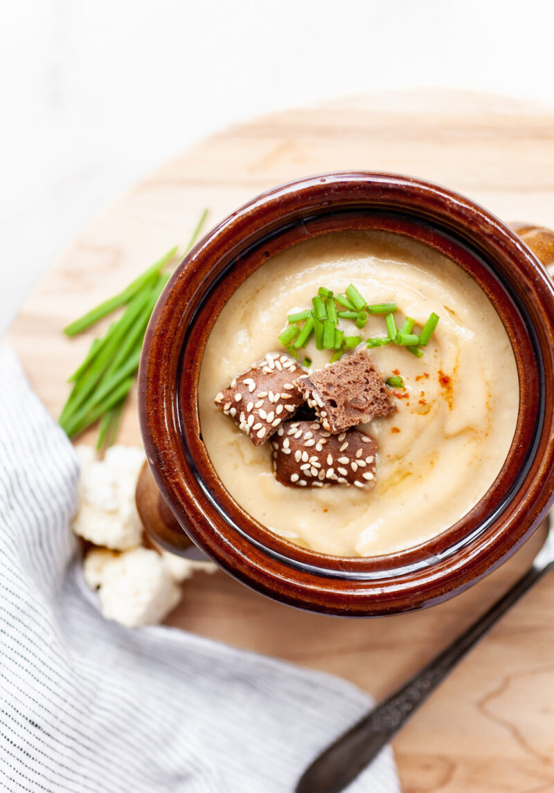 image of instant pot cauliflower soup in a rustic bowl with croutons and chives on a wood board with chives on the side