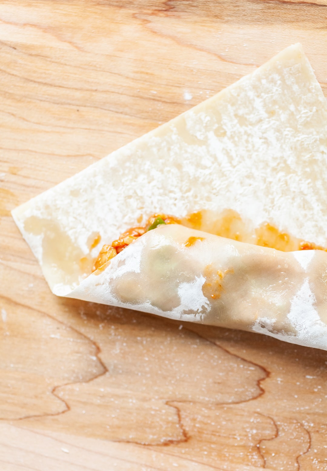 image of an egg roll wrapper being wrapped up over air fryer pizza roll ingredients