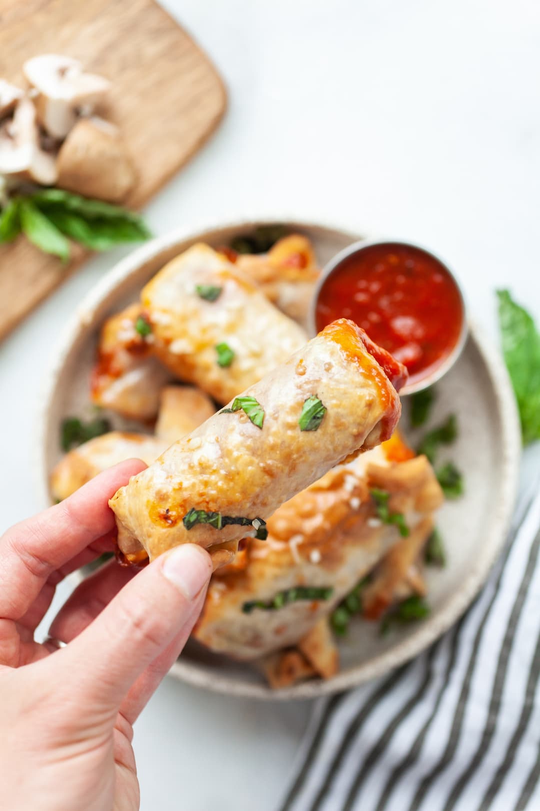 image of a hand picking up an air fryer pizza roll from a plate with more air fryer pizza rolls