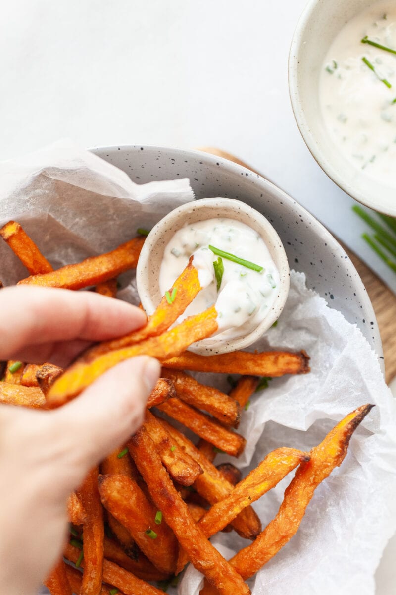 dipping cooked sweet potato fries in a small bowl of aioli dip
