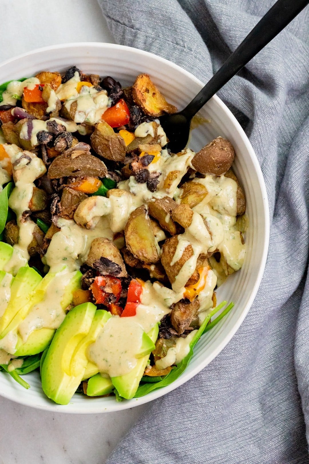 image of a bowl filled with air fryer breakfast potatoes, avocado, and vegetables, drizzled with sauce