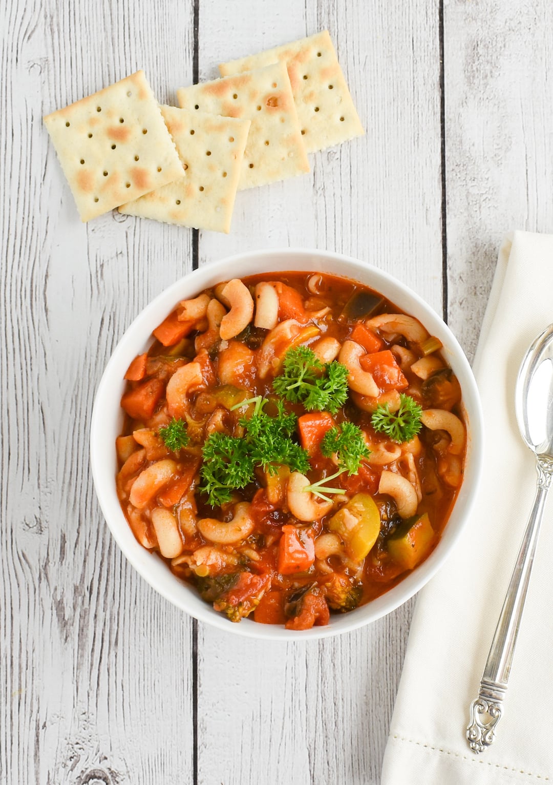 Image of a bowl of minestrone soup on a white washed wood background with crackers on the side