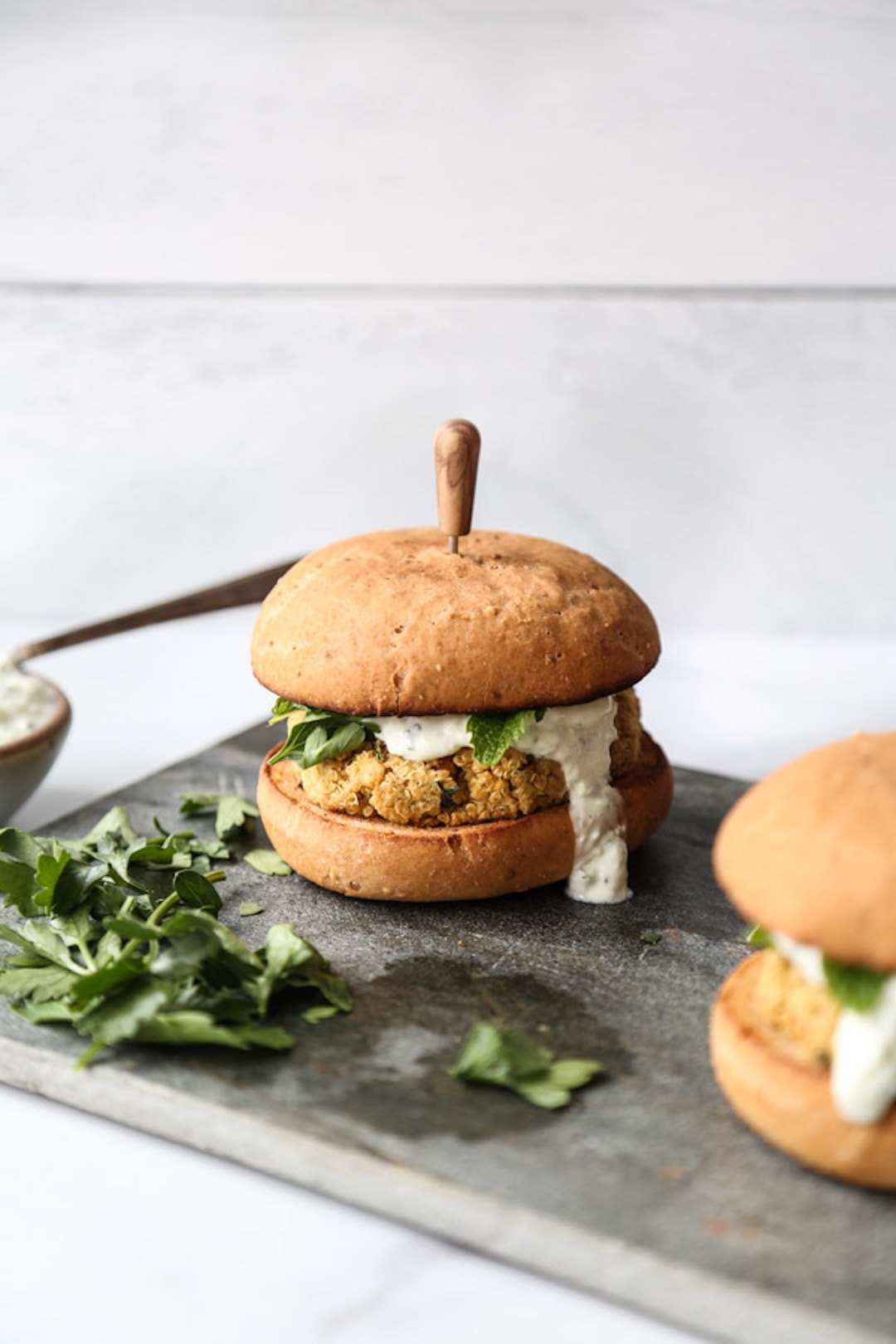 image of a chickpea burger topped with tatziki sauce sitting on a board with a white background