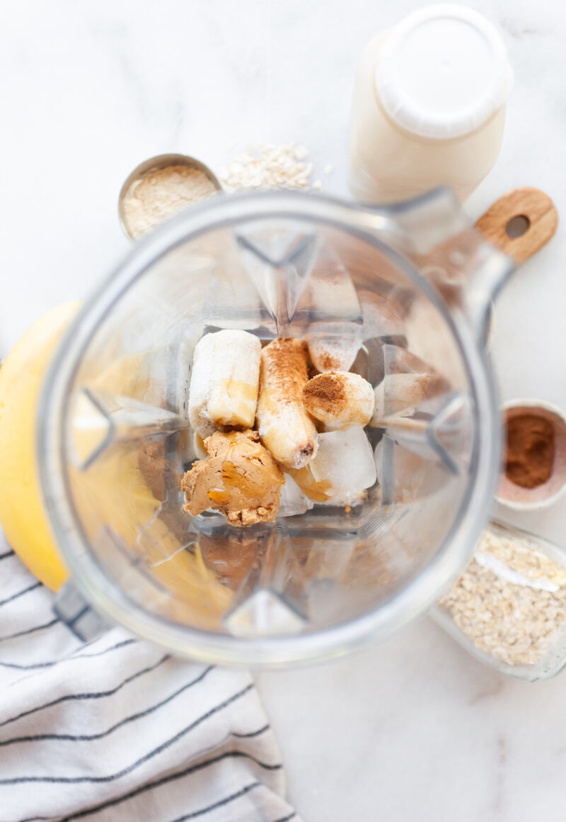 image of a vitamix canister with ingredients for oat milk smoothie inside including banana, peanut butter, and cinnamon