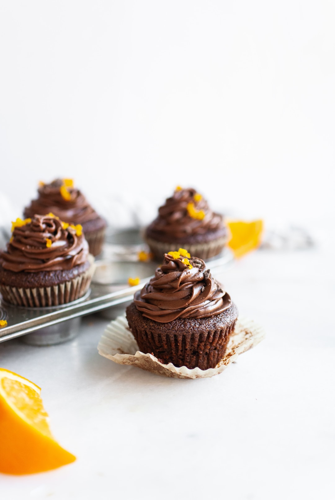 image of chocolate orange cupcakes from the side topped with orange zest and a white background
