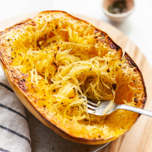 close up side angle image of an air fried spaghetti squash half sitting cut side up on a plate with a fork scooping the strands of the squash
