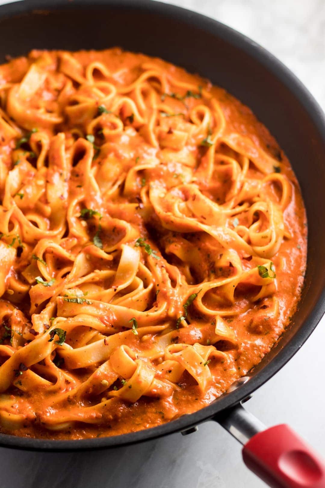 image of a close up of a pan filled with fettuccine covered in red pepper sauce