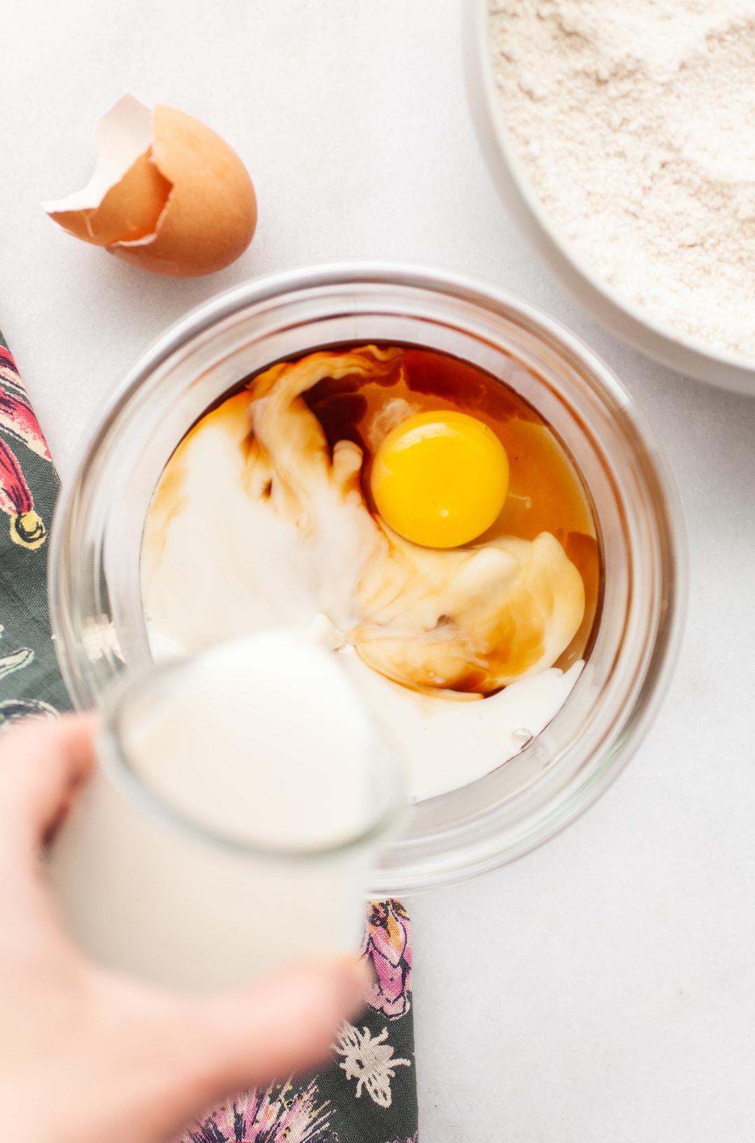 image of a glass bowl with an egg and maple syrup and almond milk being poured in