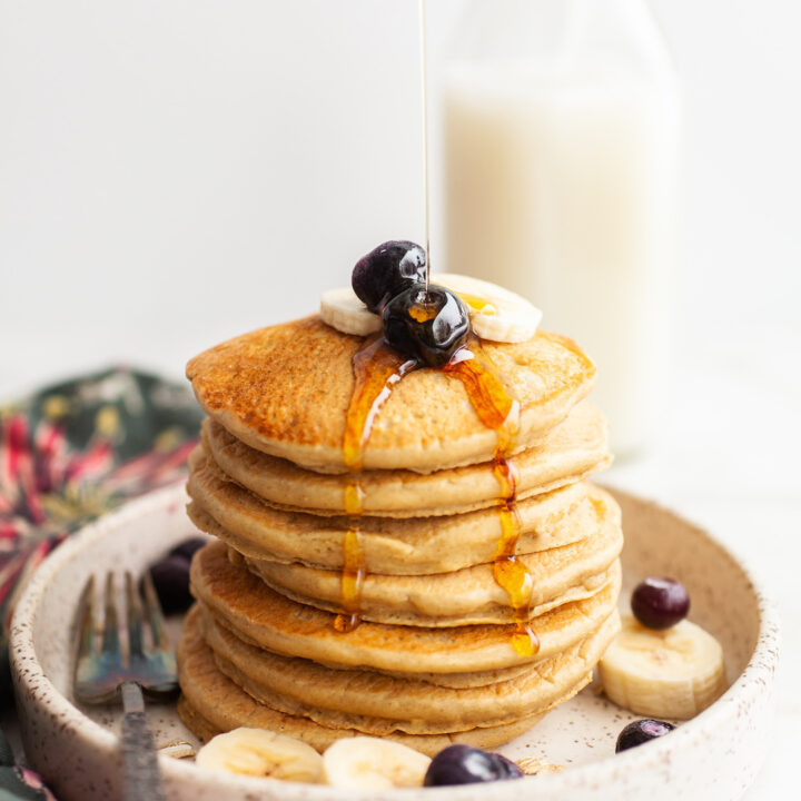 image of a stack of Fluffy Oat Flour Pancakes with maple syrup being poured on top of the stack
