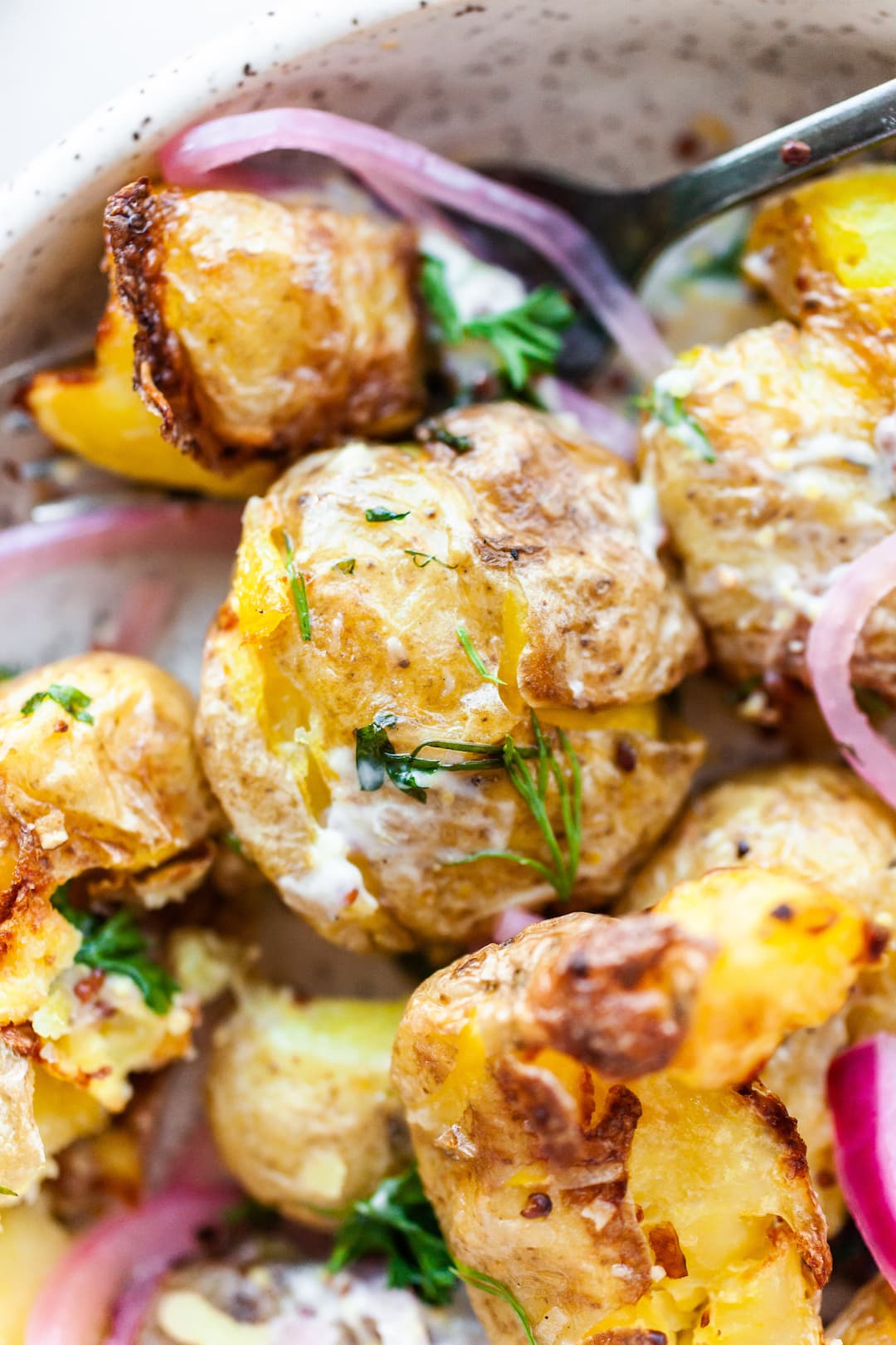image of a plate topped with air fryer smashed potatoes , herbs, and pickled red onions