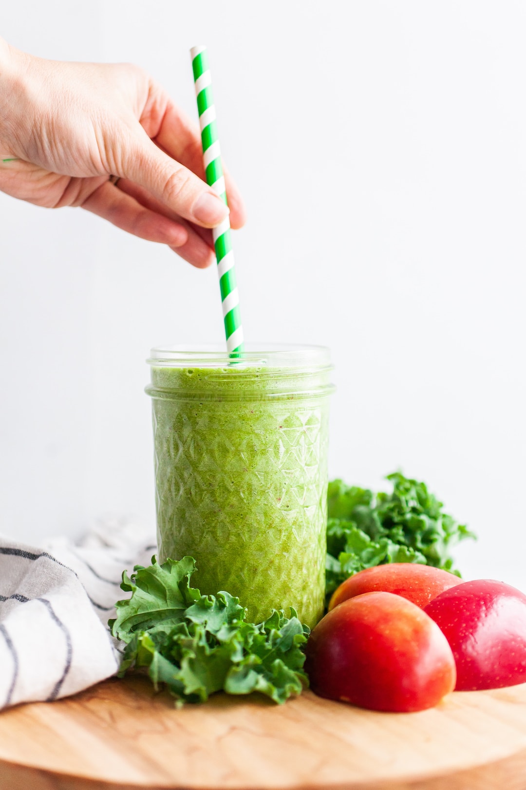 image of an apple greens smoothie against a white background with a hand putting a straw in the smoothie