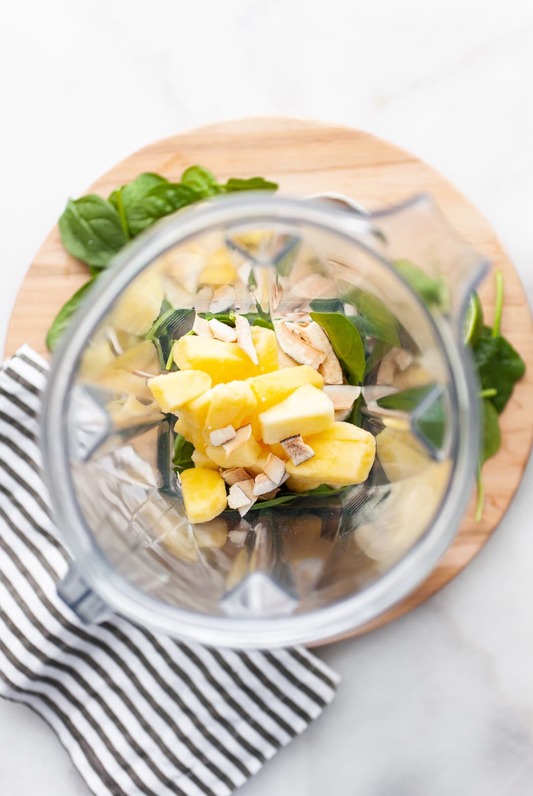image of the overhead view of a blender canister filled with frozen pineapple, spinach, banana, and coconut