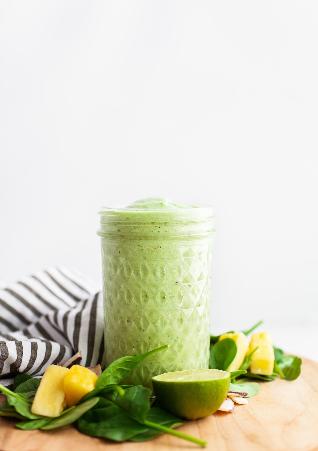 image of a glass jar filled with green smoothie on a wood board with pineapple and spinach on the side