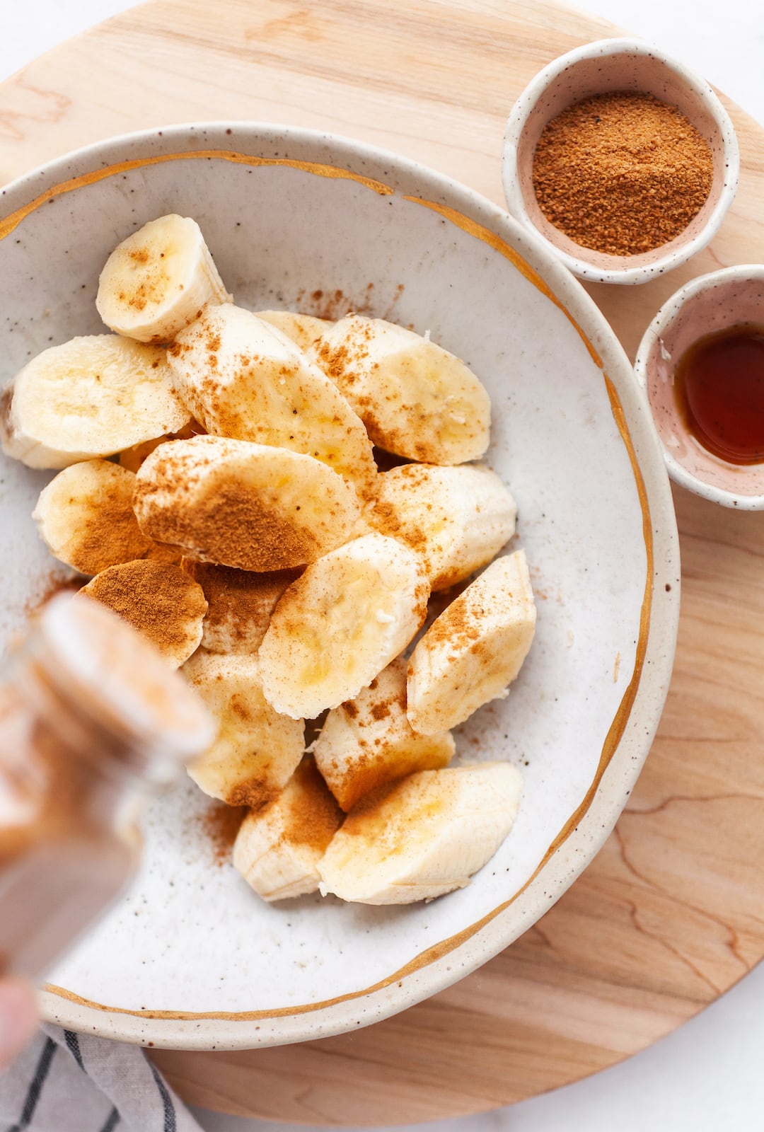image of a pottery bowl filled with banana slices being topped with cinnamon