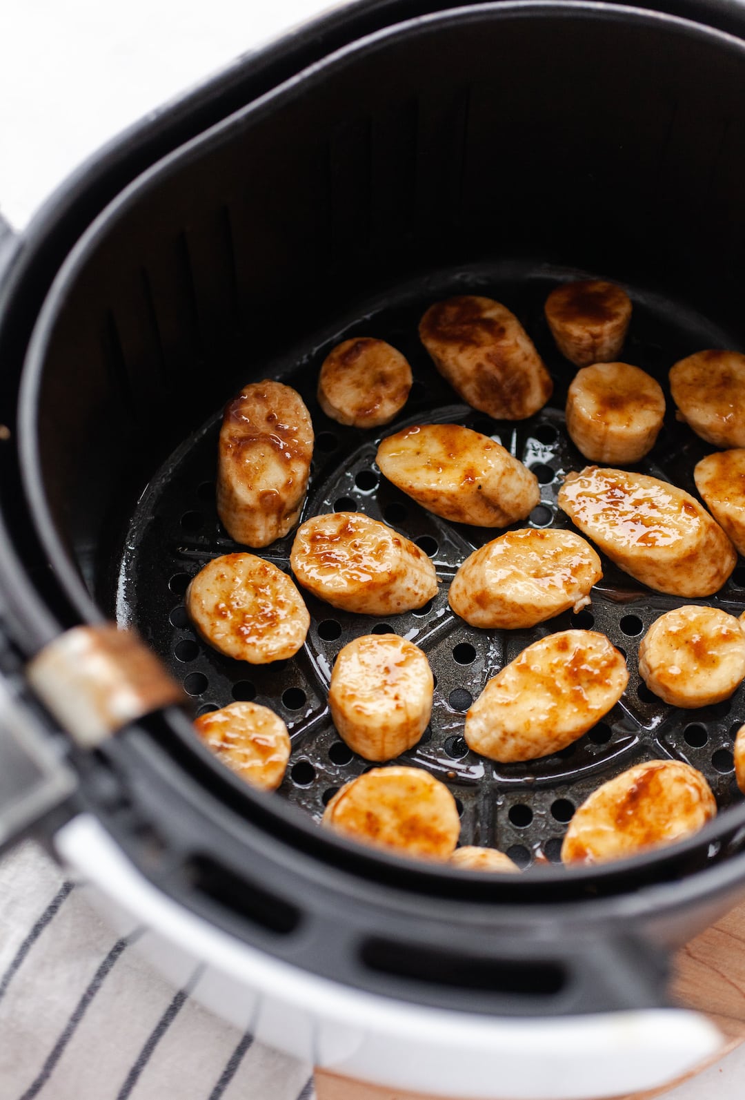 image of an air fryer basket filled with banana slices topped in cinnamon and coconut sugar